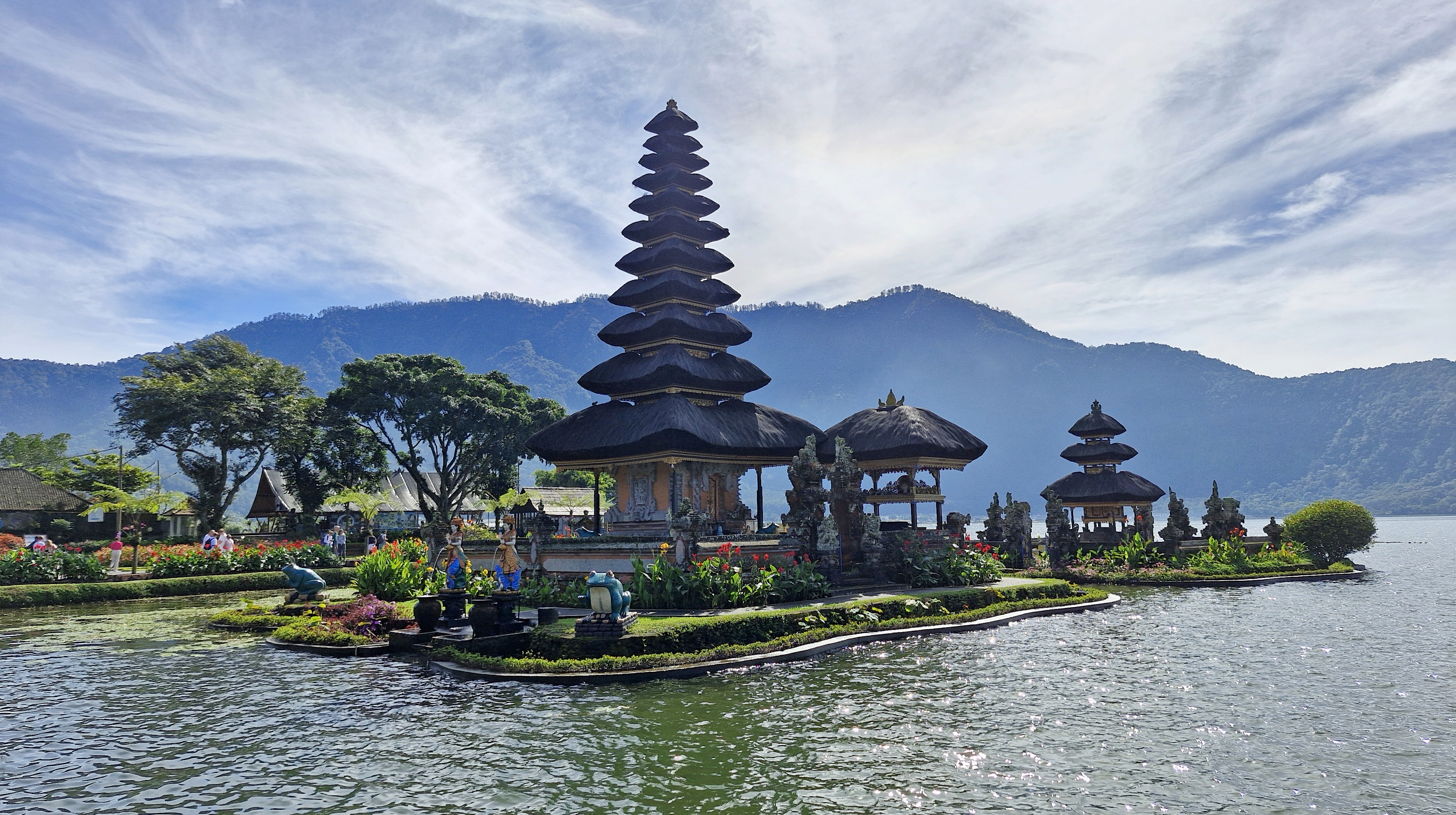 A view of Ulun Danu Beratan Temple, situated on Lake Beratan in Bali, featuring traditional Balinese architecture including multiple tiered pagodas surrounded by lush greenery and mountains in the background.