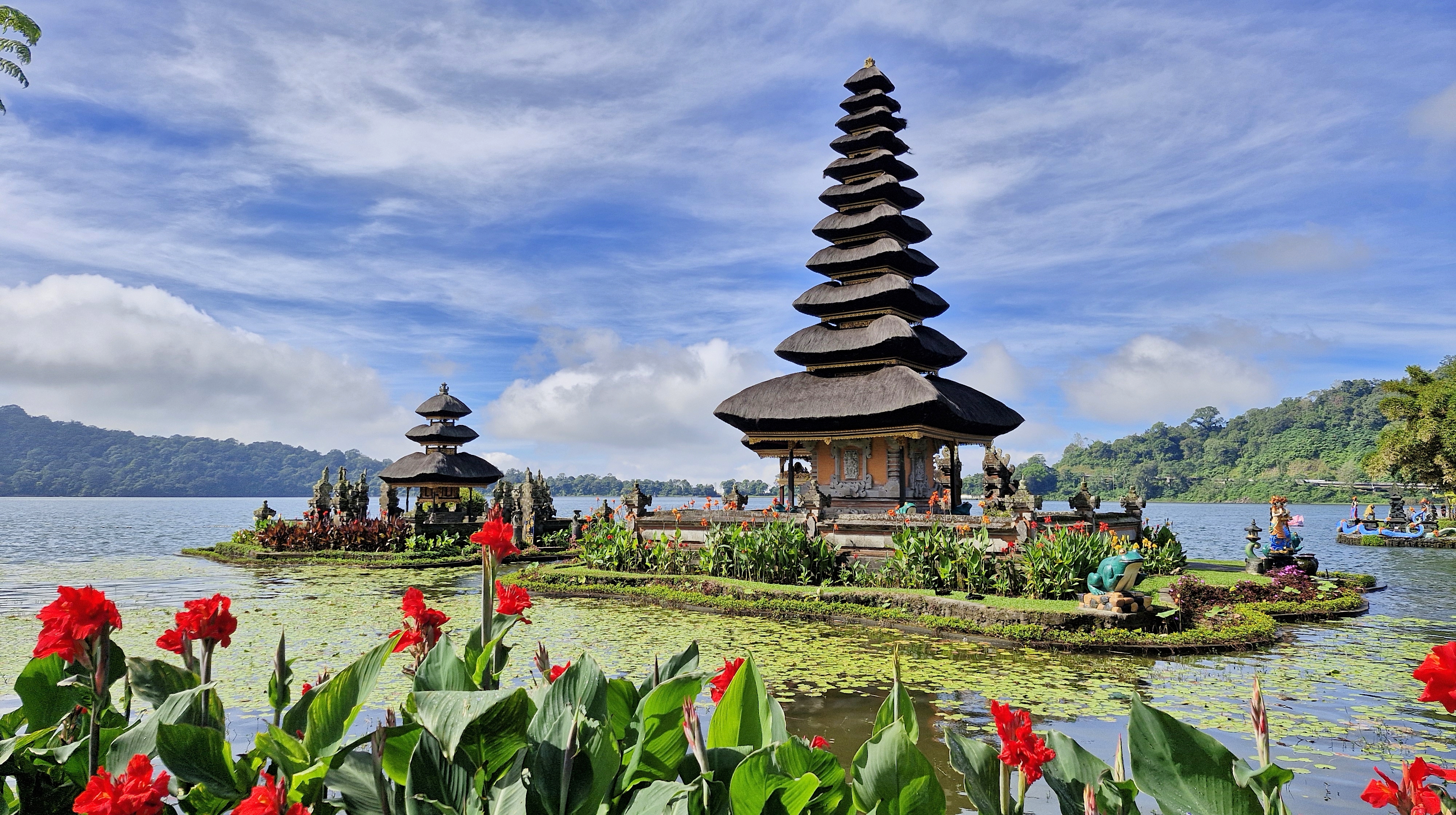 Ulun Danu Beratan temple situated on Lake Beratan, surrounded by lush greenery and vibrant flowers in the foreground.
