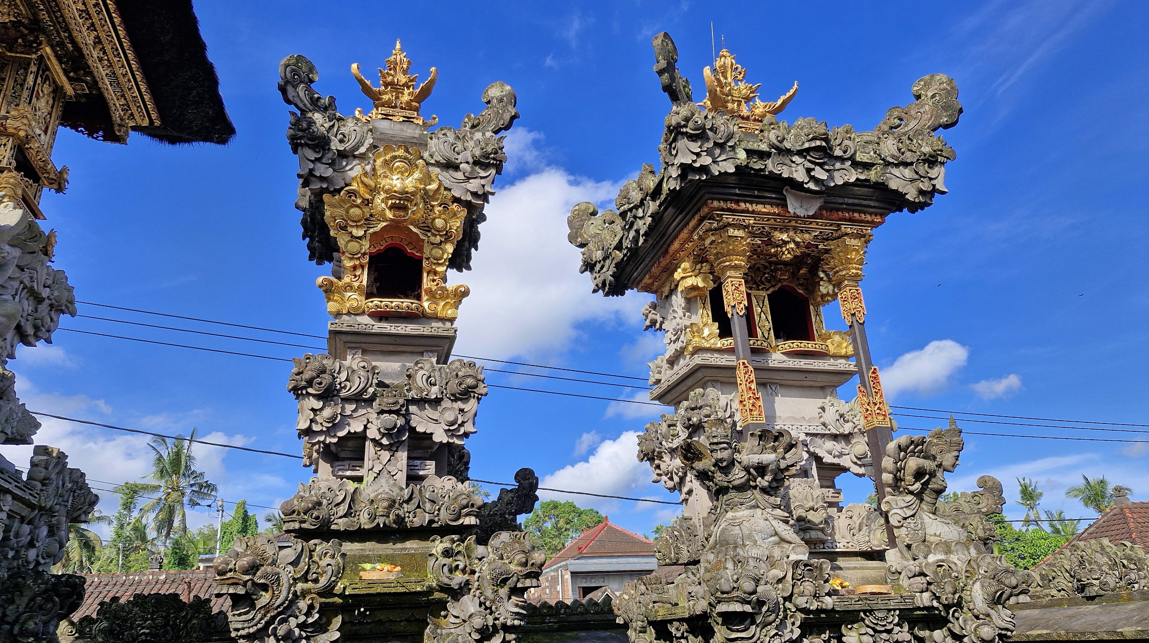 Two ornate temple towers with intricate carvings and gold accents against a blue sky.