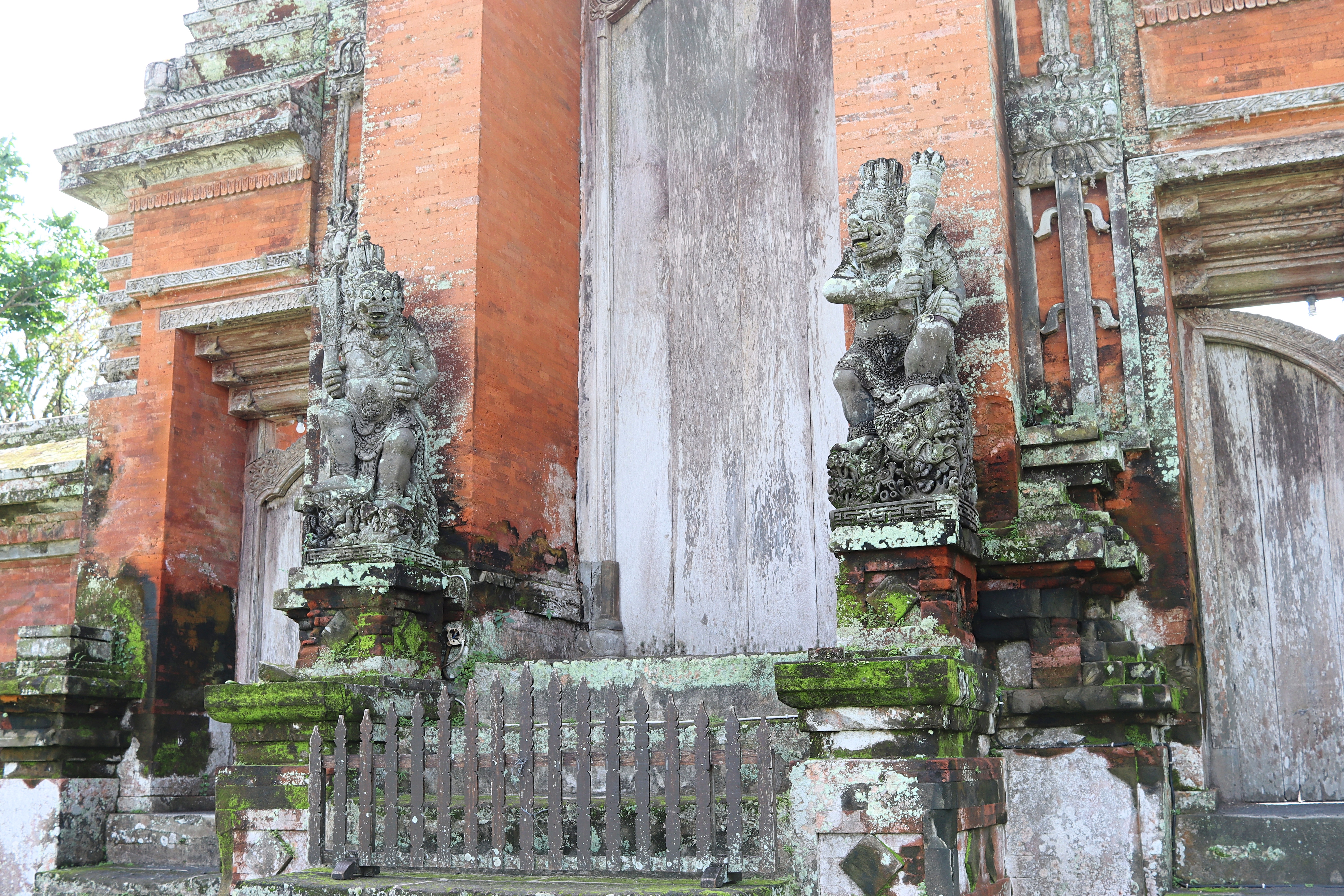 Entrance of a Balinese temple featuring ornate stone carvings and statues, with moss-covered walls.