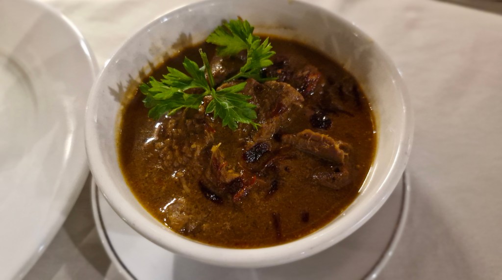 A bowl of rich beef curry garnished with fresh green herbs, placed on a white tablecloth.