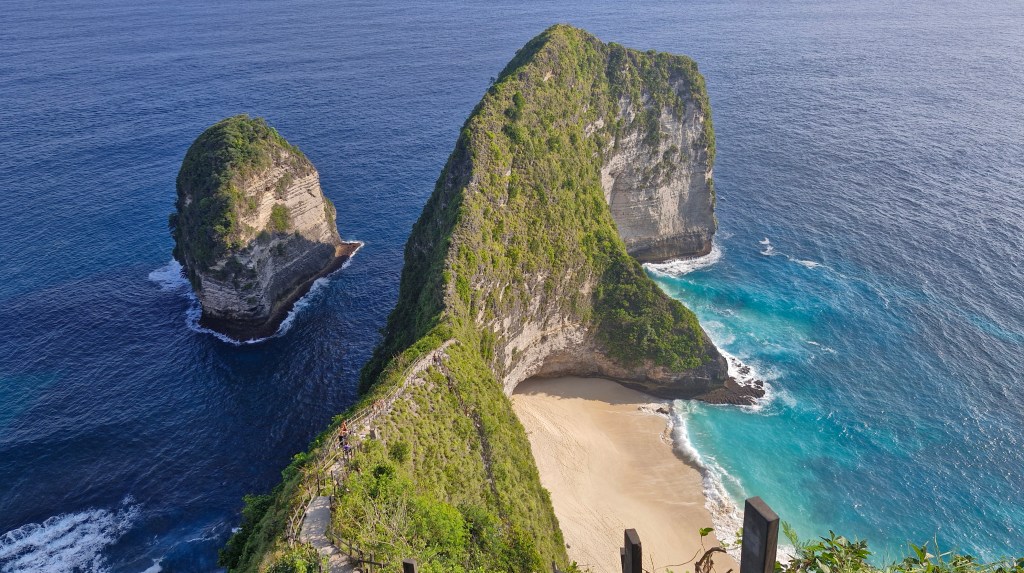 Aerial view of Kelingking Beach in Nusa Penida, featuring a distinctive T-Rex shaped cliff surrounded by turquoise waters and sandy beach.