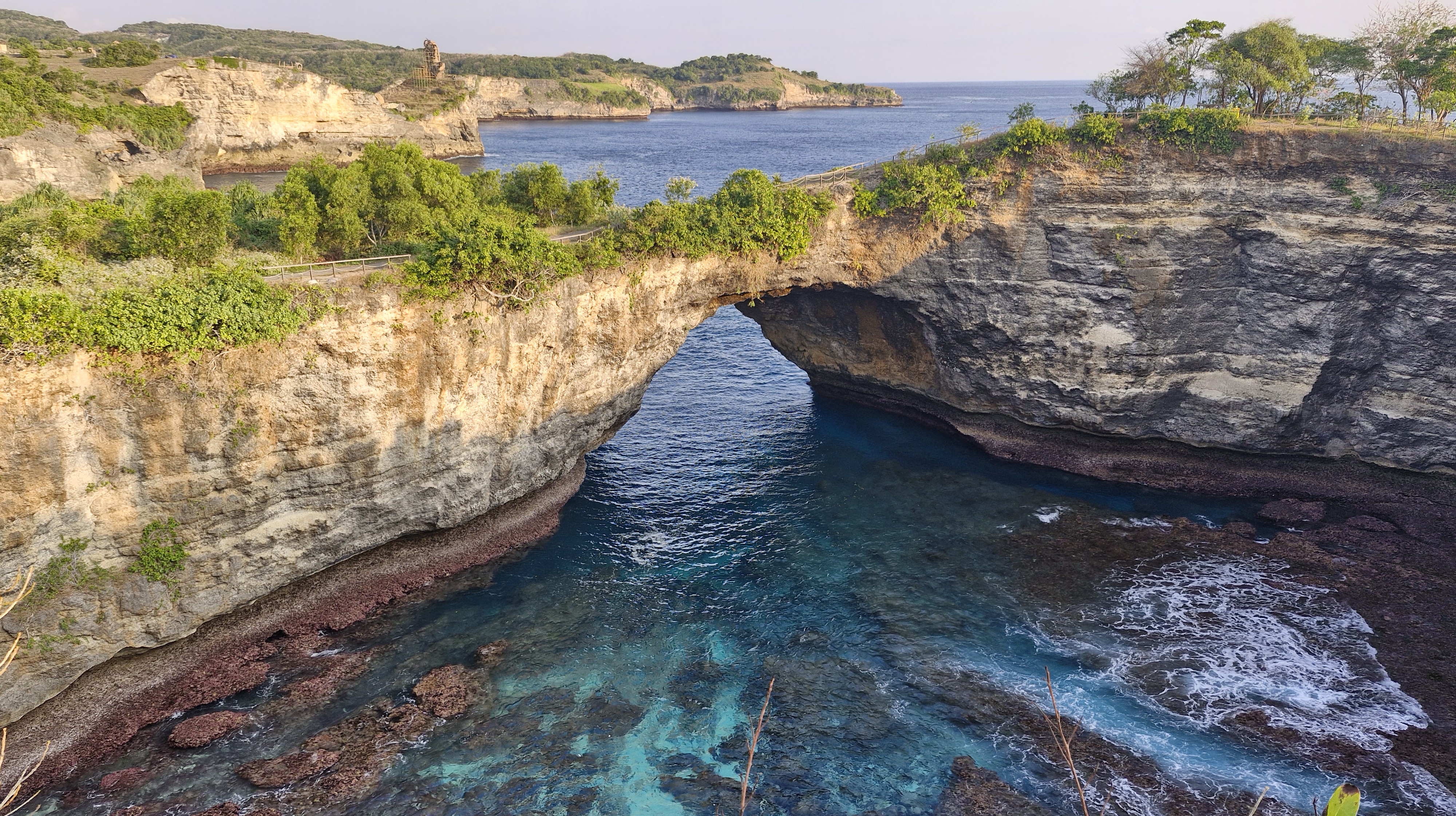 A scenic view of Broken Beach, featuring a natural rock arch with turquoise waters underneath and lush greenery surrounding the cliffs.