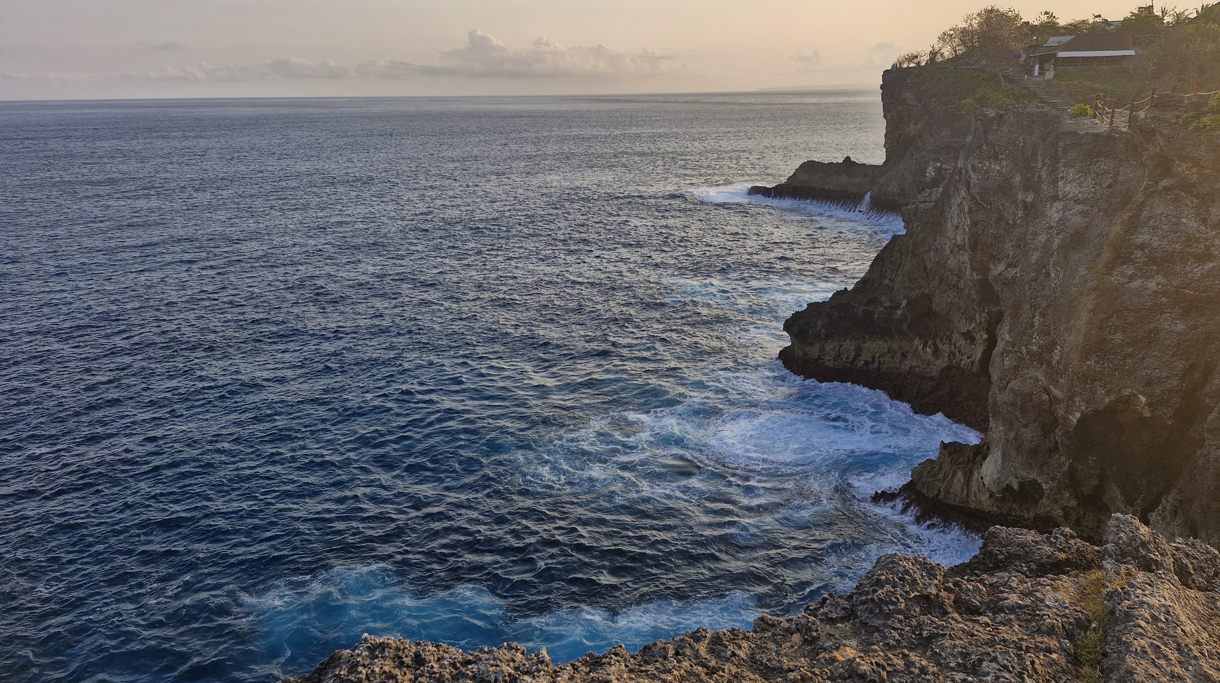 A scenic view of the ocean waves crashing against rocky cliffs during sunset on Nusa Penida.