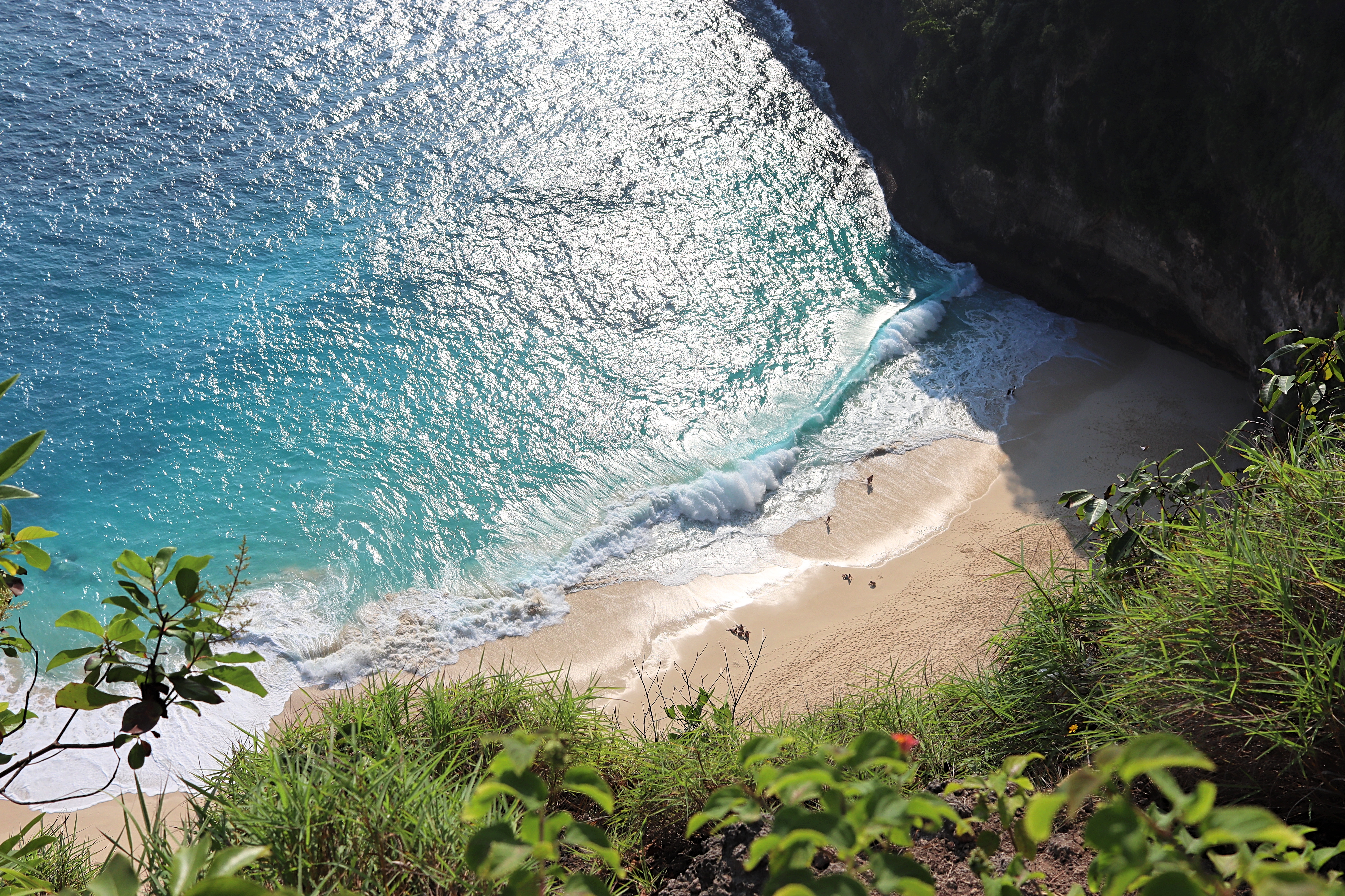 Aerial view of Kelingking Beach featuring its sandy shore and turquoise waters surrounded by steep cliffs and lush greenery.