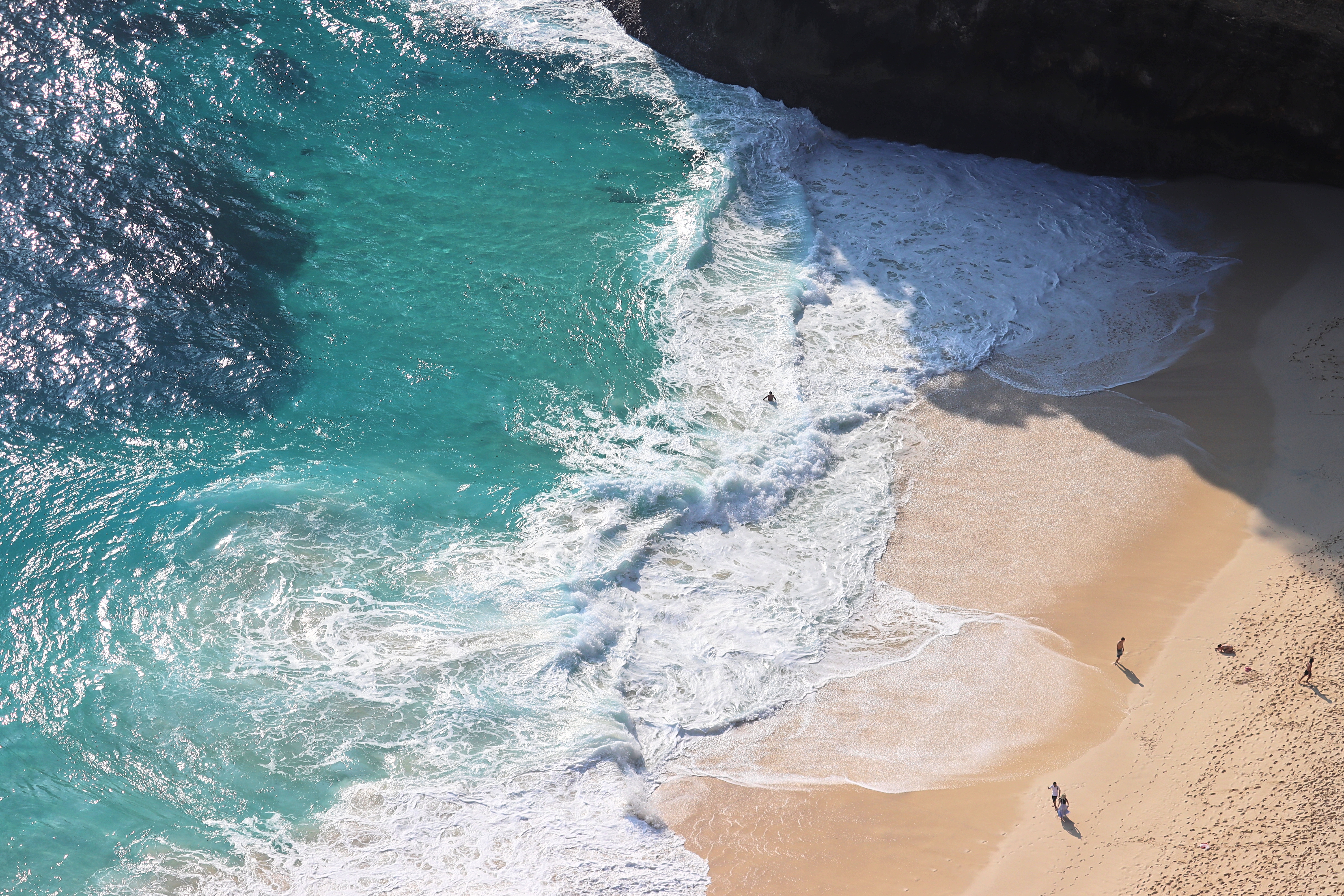 Aerial view of a stunning beach with golden sand and turquoise ocean waves crashing onto the shore, with a few people walking along the water's edge.