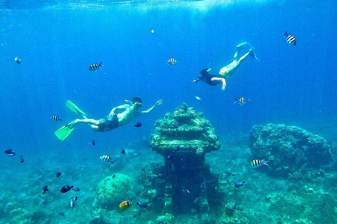 Two snorkelers exploring underwater near a small temple structure surrounded by colorful fish and coral.